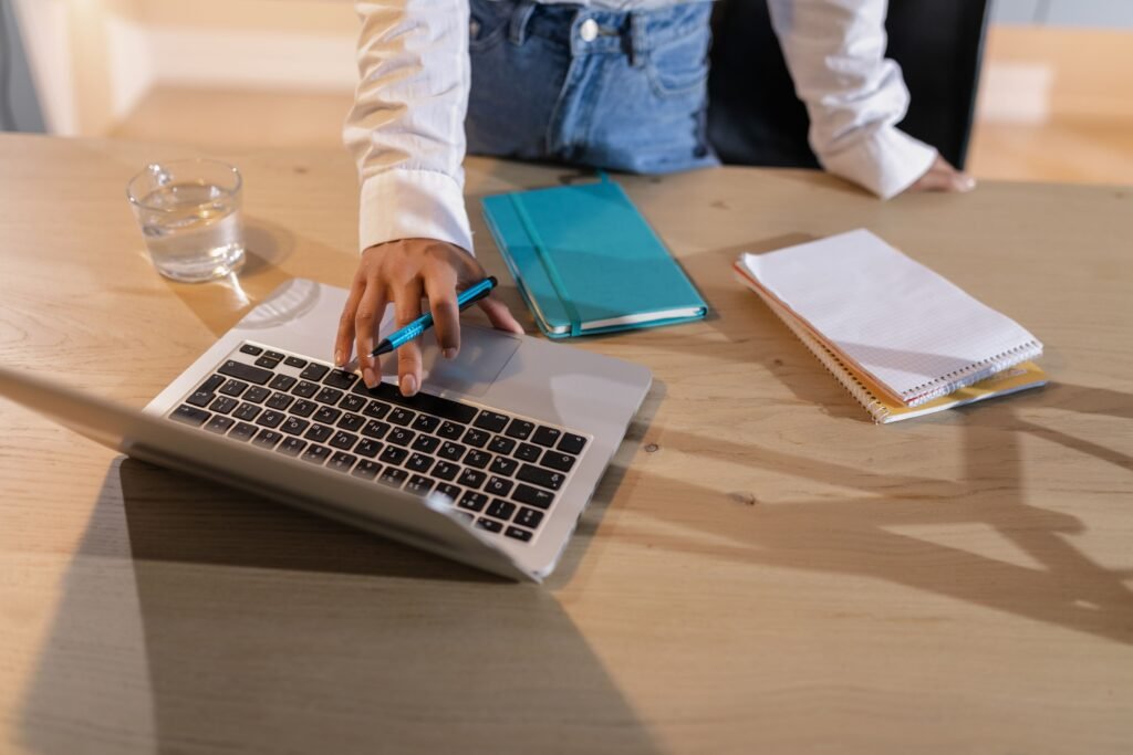 Persona escribiendo en un portátil sobre una mesa de madera con libretas y un bolígrafo