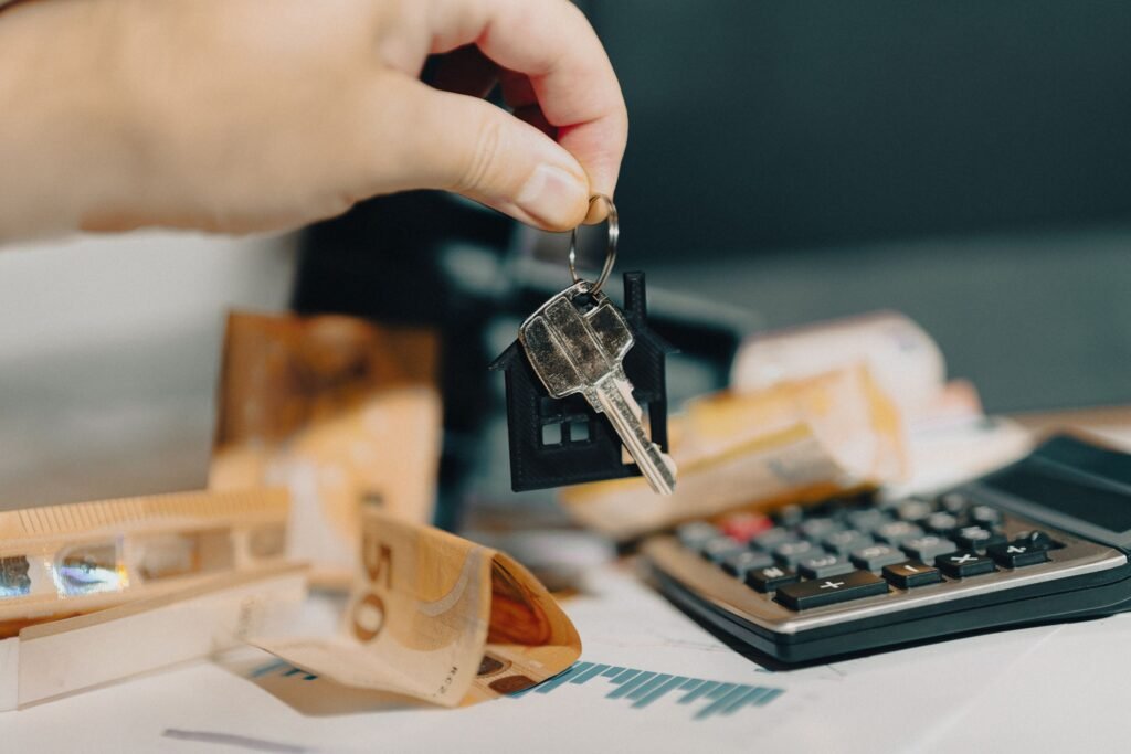 Mano sujetando las llaves de una vivienda junto a una calculadora y billetes de euro