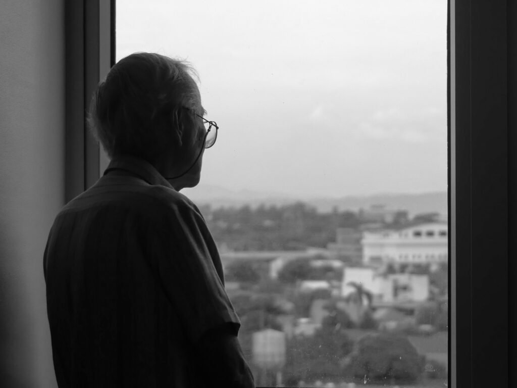 Persona mayor mirando por la ventana de su vivienda, imagen ilustrativa sobre el origen del Decreto Maricarmen