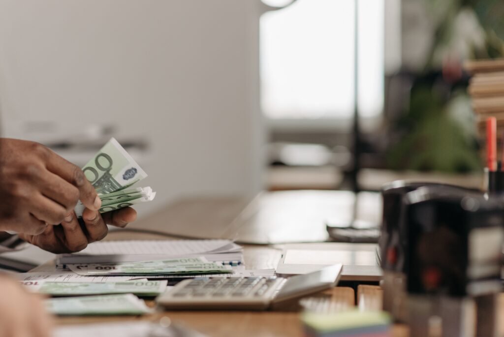 Mano contando billetes de 100 euros junto a una calculadora sobre una mesa
